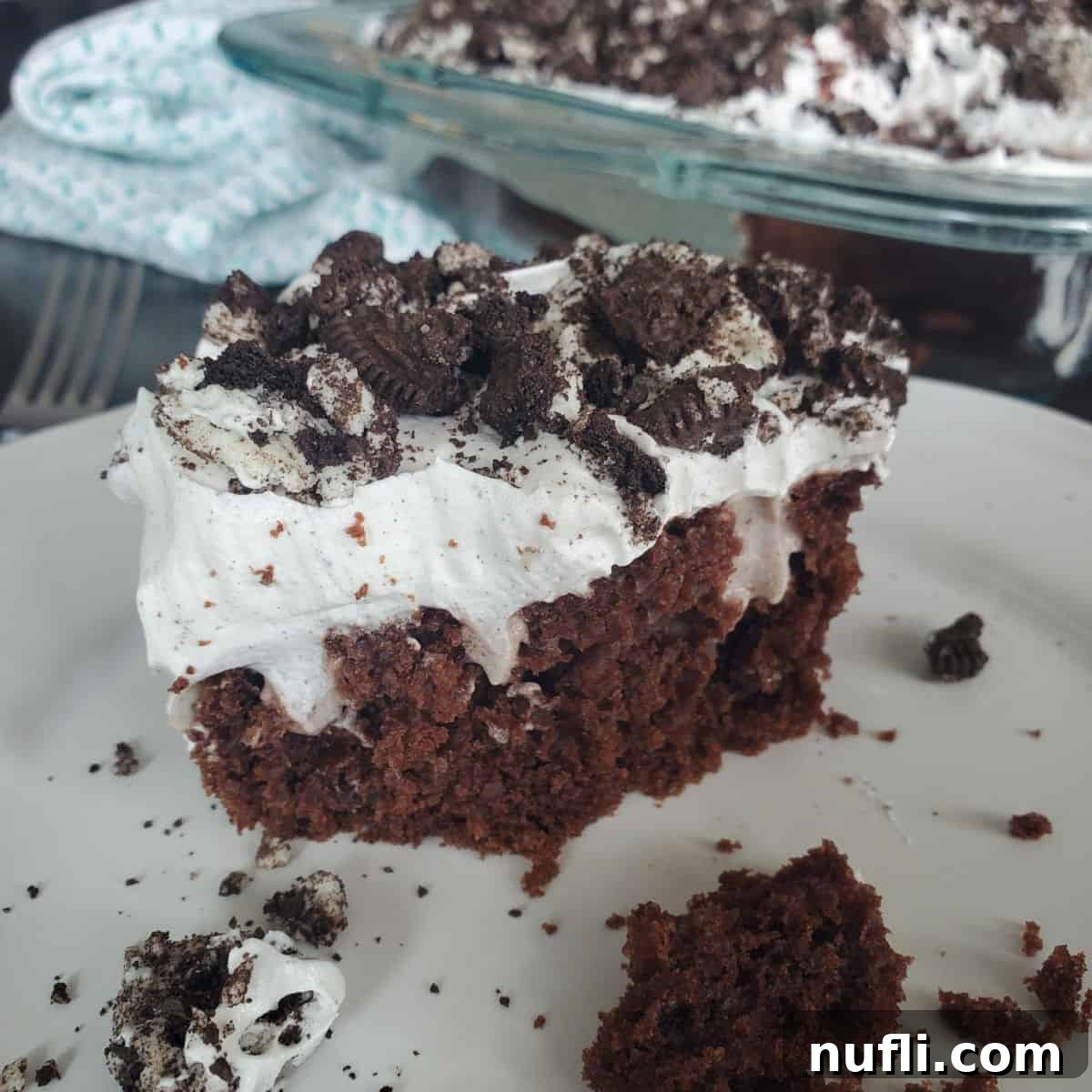 Slice of Oreo Poke Cake on a white plate next to the cake dish