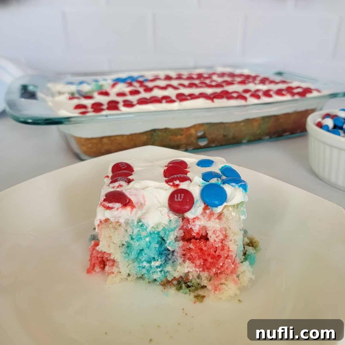 Red White and Blue Poke Cake square on a white plate next to a flag cake