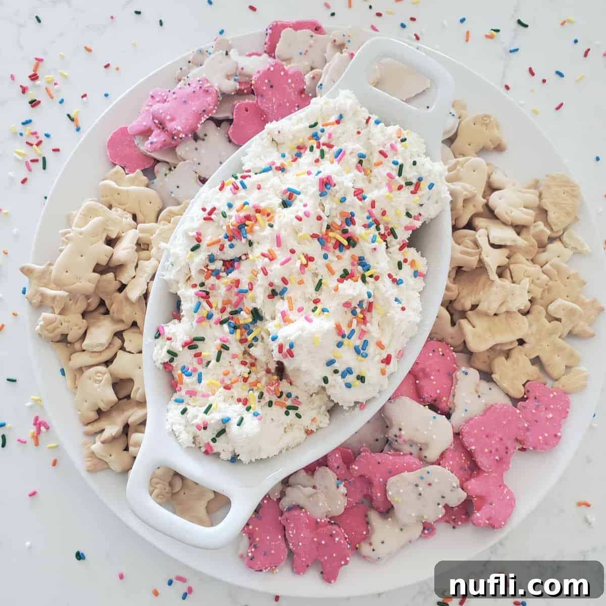 Dunkaroo dip in a white bowl surrounded by animal crackers and cookies and rainbow sprinkles