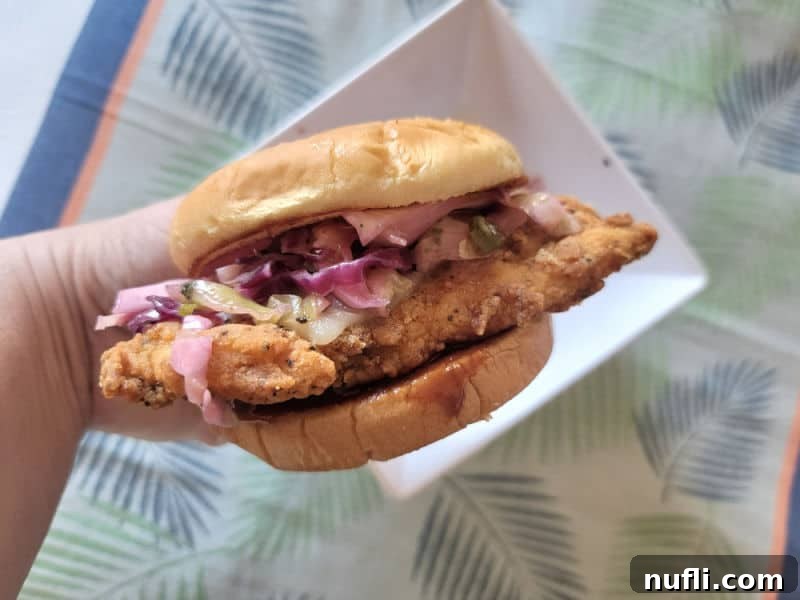 Hand holding a chicken sandwich with slaw over a white bowl and tropical napkin