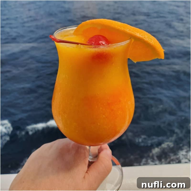 The Art of Grenadine Cocktails 6 Blended 'Kiss on the Lips' cocktail in a hurricane glass, garnished with a cherry and orange slice.