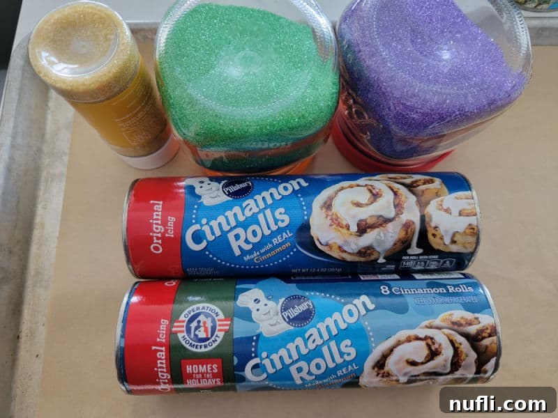 Delicious Easy Cinnamon Roll King Cake 4 Pillsbury Cinnamon Roll packages next to gold, green, and purple sprinkles, on a parchment lined baking sheet