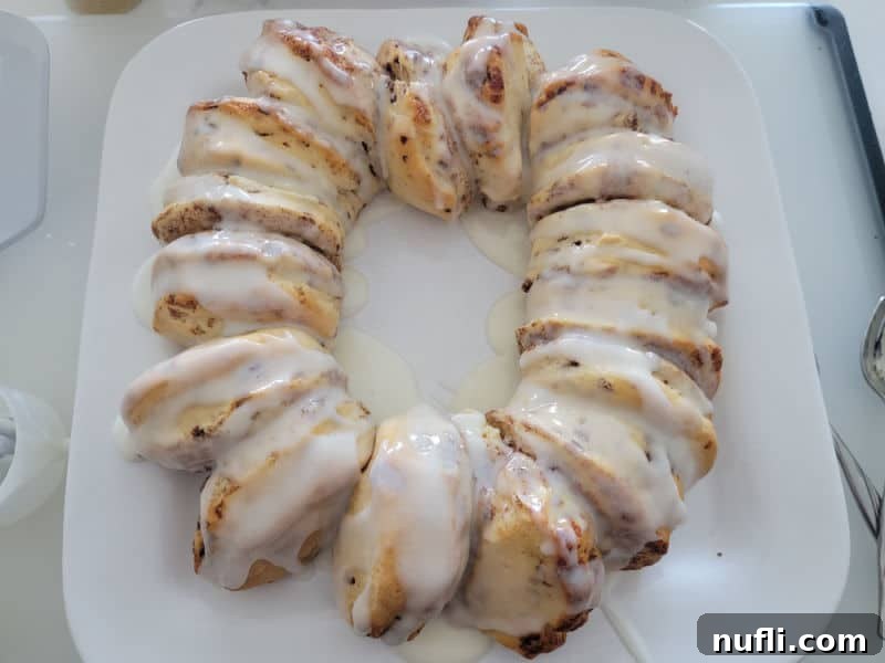 Delicious Easy Cinnamon Roll King Cake 7 icing covering cinnamon rolls in a circle on a white plate