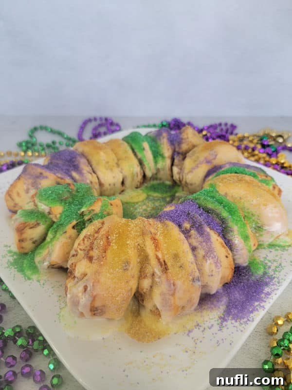 Delicious Easy Cinnamon Roll King Cake 9 Mardi gras cinnamon roll king cake on a white plate surrounded by mardi gras beads