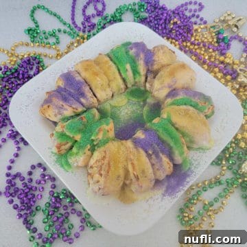 Delicious Easy Cinnamon Roll King Cake 10 Cinnamon Roll King Cake on a white platter surrounded by Mardi Gras Beads