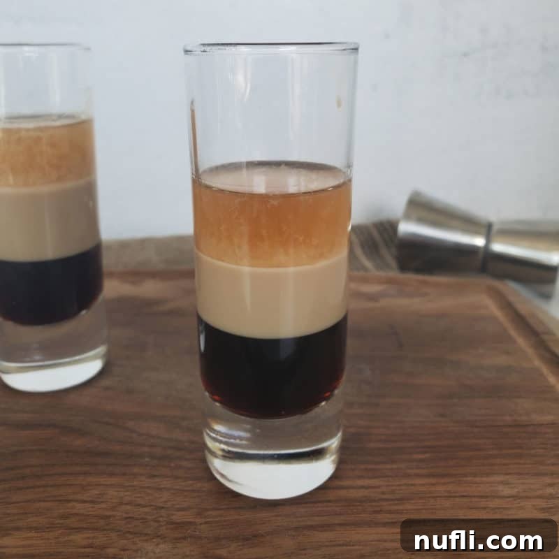 Duck Fart Shot layered in a shot glass sitting on a wood cutting board with a cocktail jigger.