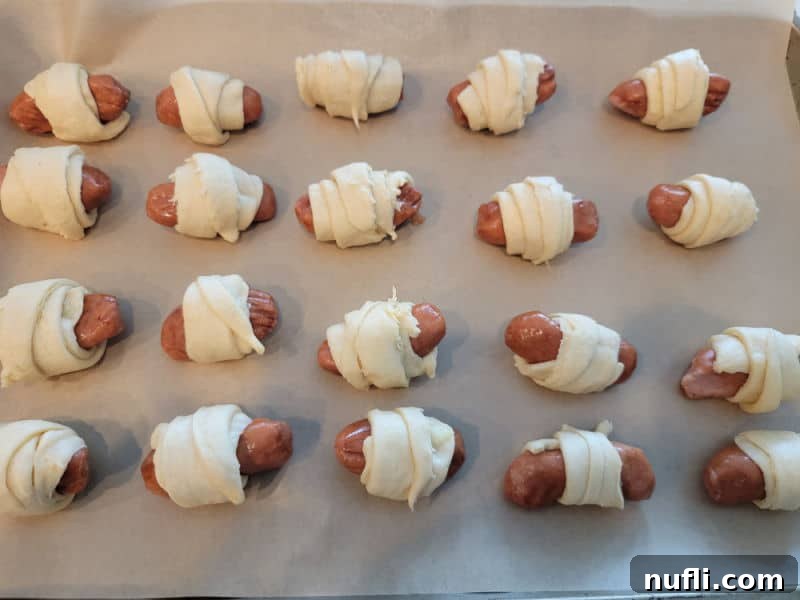 Petite Sausage Parcels 6 unbaked pigs in a blanket lined up on a parchment lined baking sheet