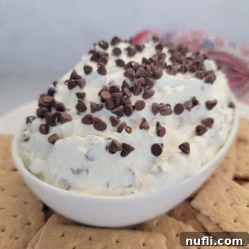 Booty dip covered in mini chocolate chips in a white bowl surrounded by graham crackers