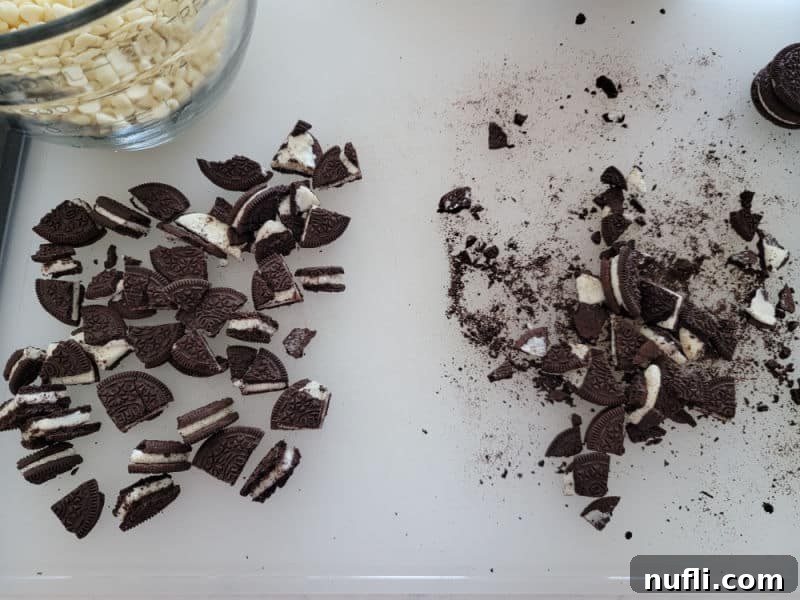 Effortless Two-Ingredient Oreo Bark 4 Pile of broken Oreo cookie pieces and a bowl of white chocolate chips on a cutting board, ready for melting.