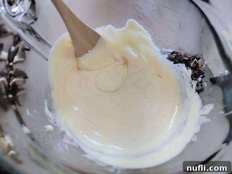 Effortless Two-Ingredient Oreo Bark 5 Smooth, melted white chocolate in a glass bowl, ready for mixing, with a wooden spoon.