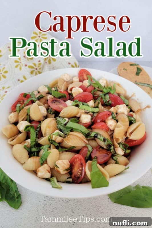 Vibrant Italian Pasta Salad 2 Caprese Pasta Salad on a white plate with pasta shells, tomatoes, mozzarella, and basil strips next to a wooden spoon and cloth napkin, highlighting its fresh and inviting presentation.