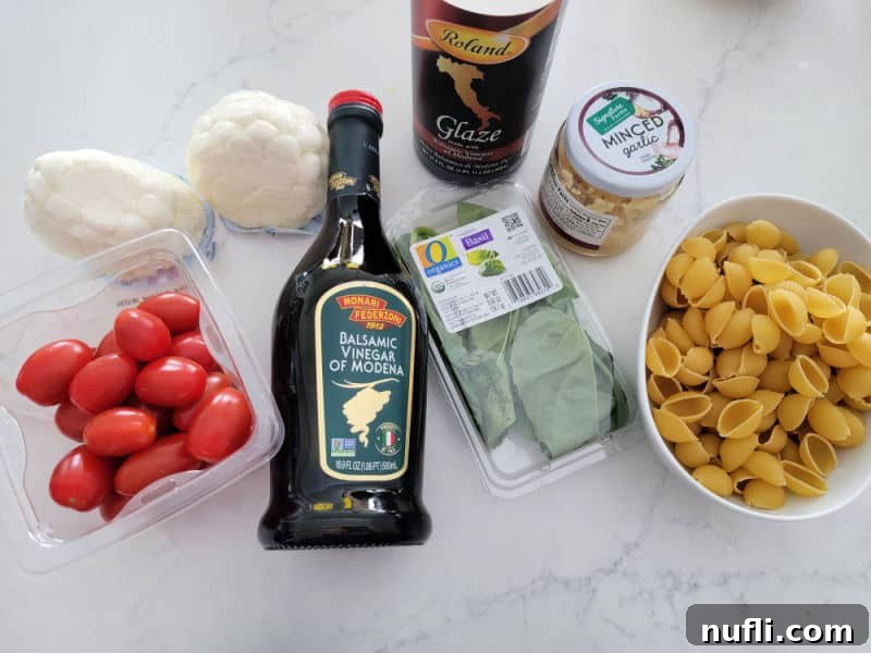 Vibrant Italian Pasta Salad 3 Close-up of fresh ingredients: cherry tomatoes, mozzarella balls, olive oil, balsamic glaze, fresh basil, and minced garlic, ready to be combined with pasta shells in a bowl on a white counter.