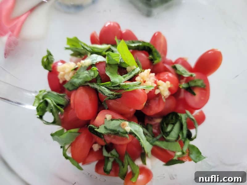Vibrant Italian Pasta Salad 4 Cut cherry tomatoes, minced garlic, and thinly sliced basil strips in a clear glass bowl, showcasing the fresh herbs and vegetables.