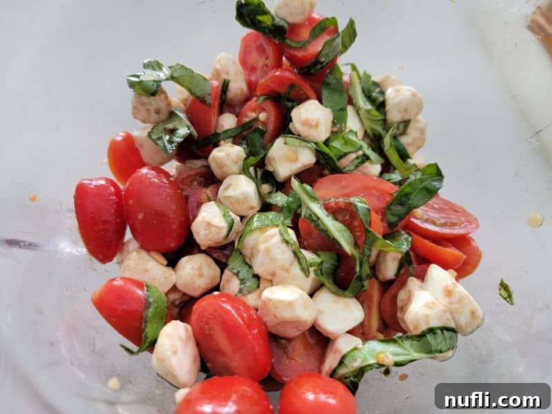 Vibrant Italian Pasta Salad 5 Mozzarella balls, cut cherry tomatoes, and basil strips in a glass bowl, illustrating the colorful and fresh core ingredients.