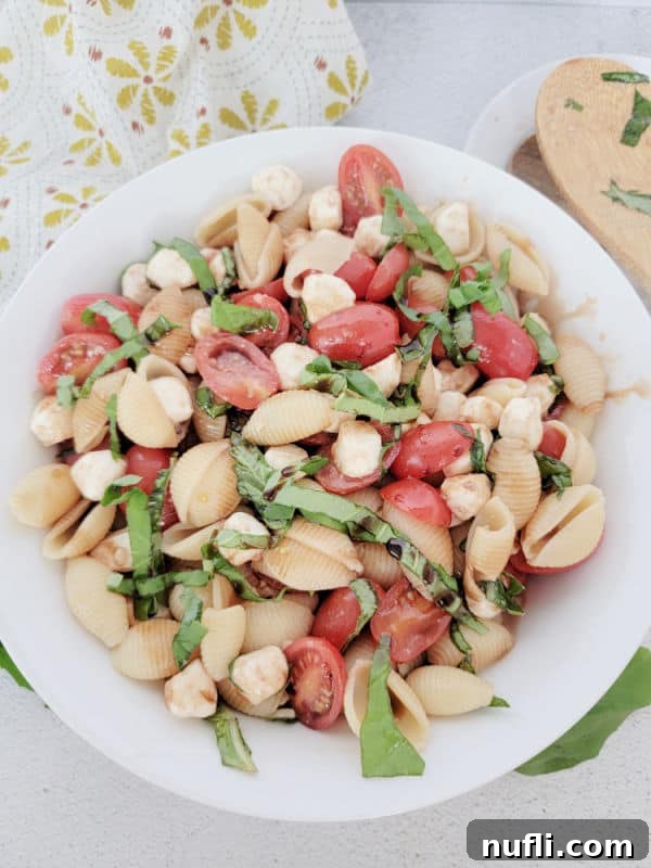 Vibrant Italian Pasta Salad 7 Caprese pasta salad in a white bowl with a wooden spoon and cloth napkin, elegantly plated for serving.