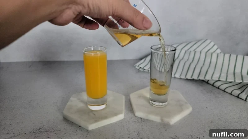 Hand pouring Jameson Irish Whiskey into a shot glass next to a shot glass with orange juice