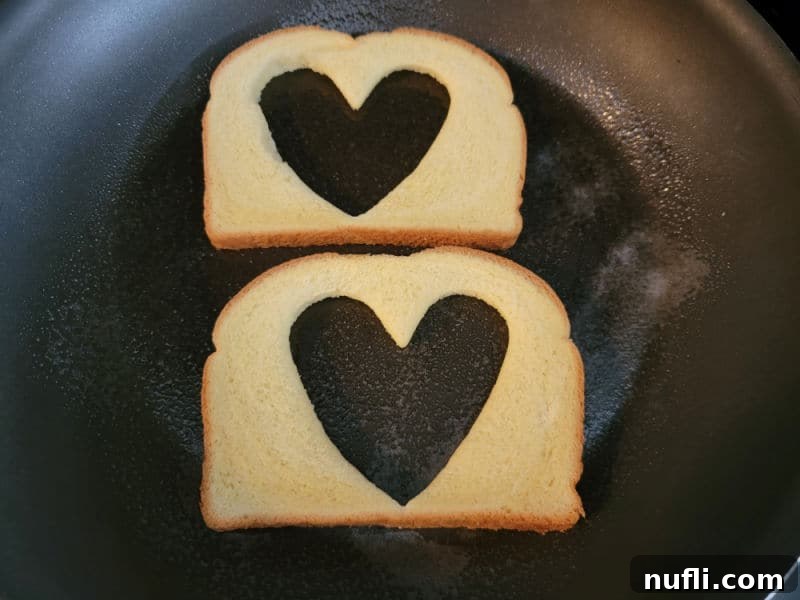 Two pieces of bread with a heart cut out of them in a skillet