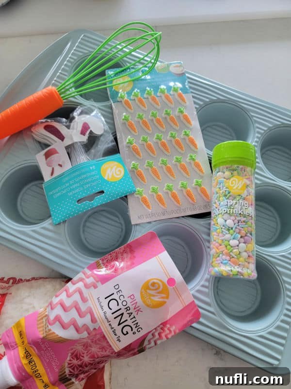 Hoppy Cupcake Delights 3 A collection of Easter baking supplies including a blue cupcake pan, glitter bunny ears, a cute carrot whisk, pastel candies, sprinkles, and pink icing, all laid out on a clean white counter.