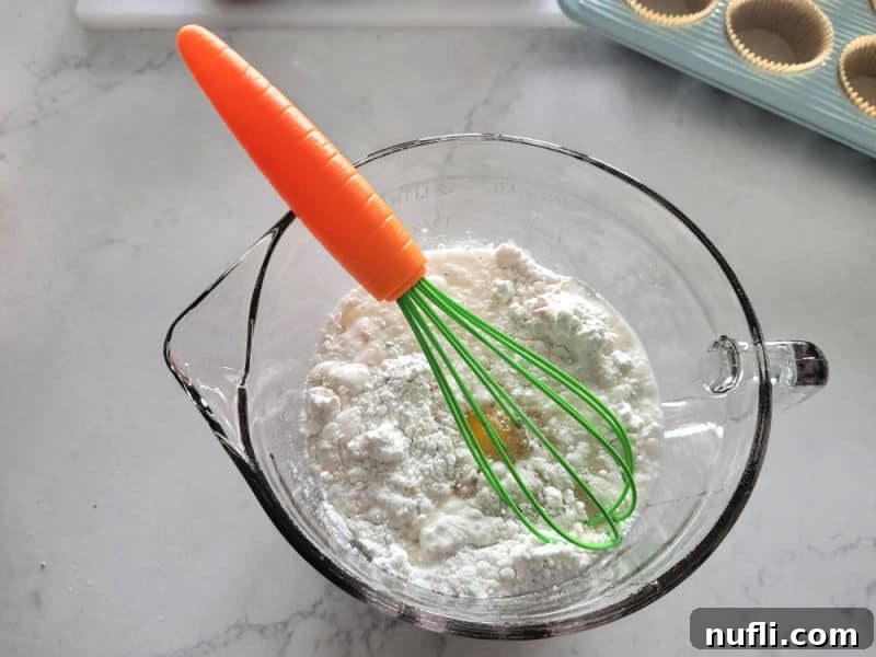 Hoppy Cupcake Delights 4 A playful carrot-shaped whisk stirring vibrant yellow cake batter in a clear glass mixing bowl, showcasing the fun of baking.