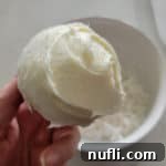 Hoppy Cupcake Delights 5 A freshly baked cupcake generously covered in smooth white icing, being held above a bowl brimming with shredded coconut, ready for its transformation into a bunny.