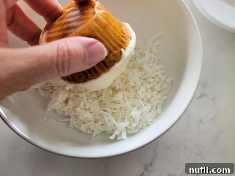Hoppy Cupcake Delights 6 A hand gently dipping and rolling a generously frosted cupcake into a bowl filled with shredded coconut, aiming for complete and even coverage.