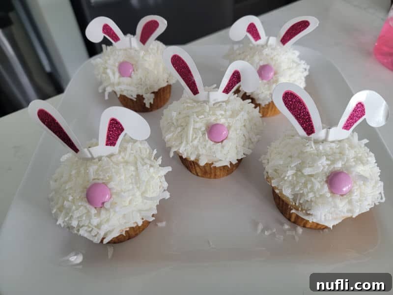 Hoppy Cupcake Delights 8 A charming line-up of finished bunny cupcakes, each adorned with glittery ears and a pink candy nose, beautifully arranged on a white platter.