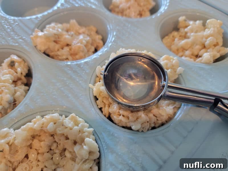 Cookie scoop pushing rice krispie treats into a muffin tin