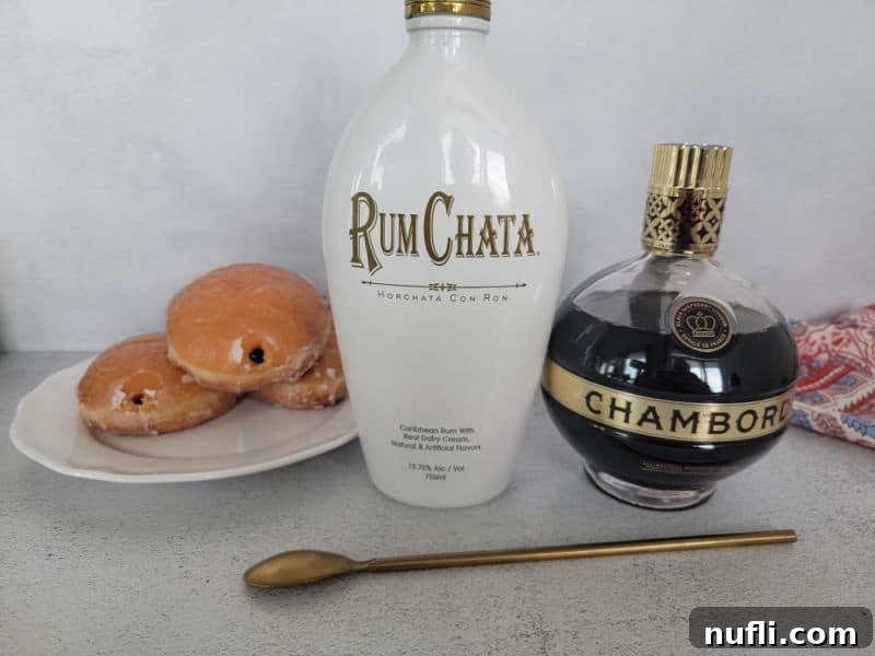 Jelly doughnuts on a white plate next to bottles of RumChata and Chambord, with a gold bar spoon, showcasing the ingredients for the shot.