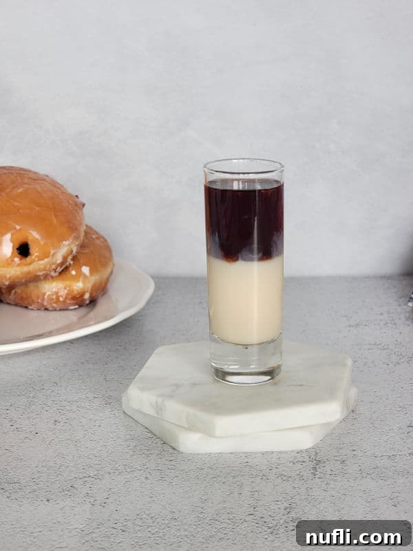 Layered purple and cream shot on white coasters next to a white plate with jelly doughnuts, showing the finished product.