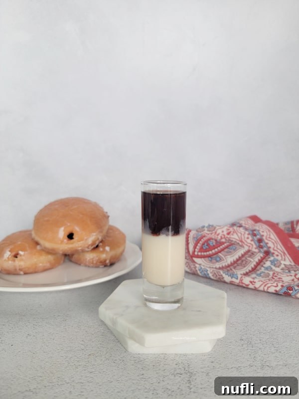 Layered shot sitting on white coasters next to a plate of jelly donuts and a cloth napkin, showcasing a perfectly executed drink.