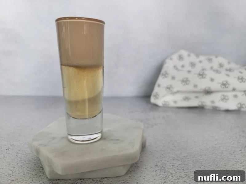 A perfectly layered Nutty Irishman cocktail shot on two white coasters with a textured cloth napkin in the background, highlighting the distinct beverage layers.