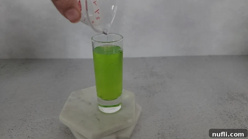 Shot glass filled with green liquid sitting on white coasters.