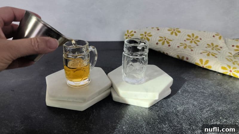 Hand pouring Licor 43 into a mini beer glass sitting on a coaster. 