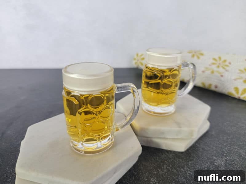Two mini beer shots on white marble coasters with a cloth napkin in the background. 