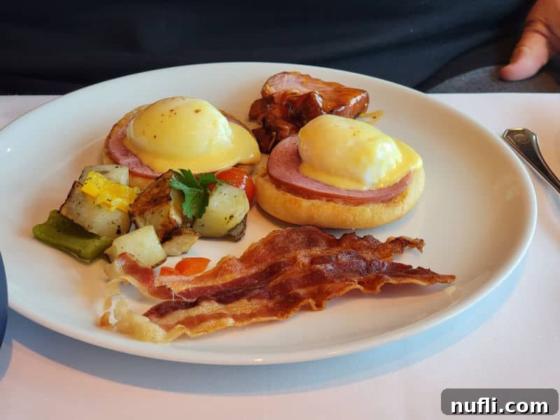 Eggs benedict, bacon, and potatoes on a white plate