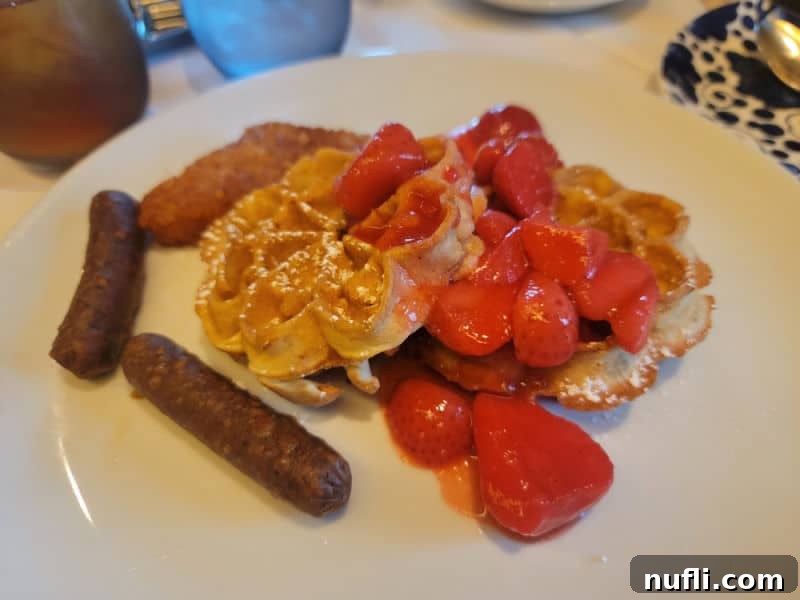 A delightful breakfast plate featuring waffles with fresh strawberries, accompanied by savory sausage, served on a crisp white plate.