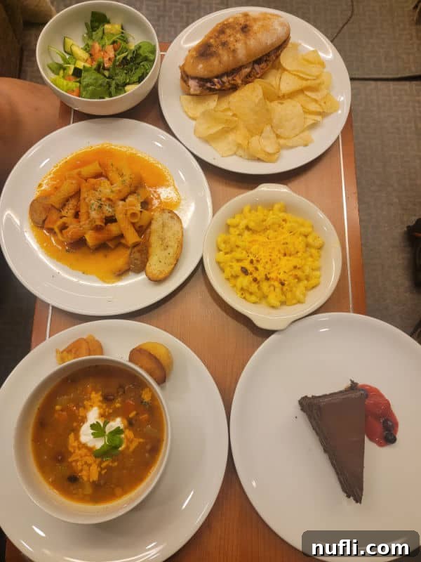 Table covered in white plates with a sandwich, soup, pasta, chocolate cake, and a salad