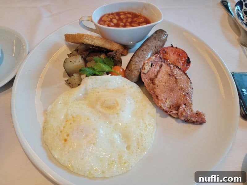 White plate with ham, sausage, eggs, baked bean, and potatoes. 