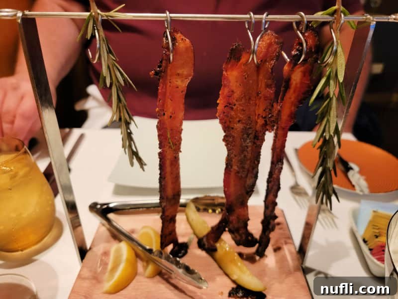 Bacon hanging from a metal rack with rosemary and lemon