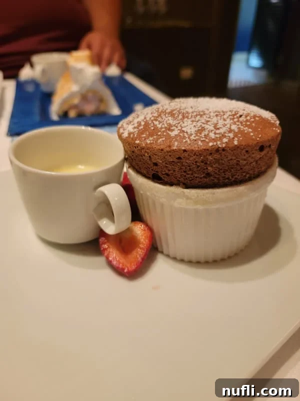 An exquisite Chocolate Souffle served in a white bowl, accompanied by a cup of cream and fresh strawberries, a luxurious dessert.