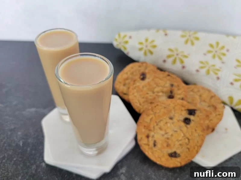 Two cocktail shots on a white coaster next to a stack of oatmeal cookies and a cloth napkin