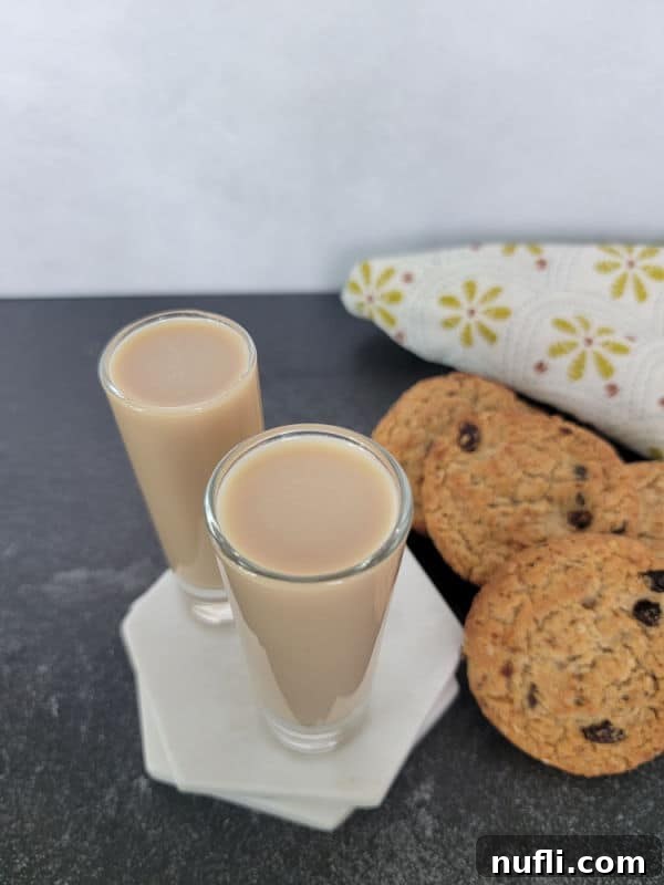 Two cocktail shots on a white marble coaster next to a stack of oatmeal cookies and a cloth napkin 