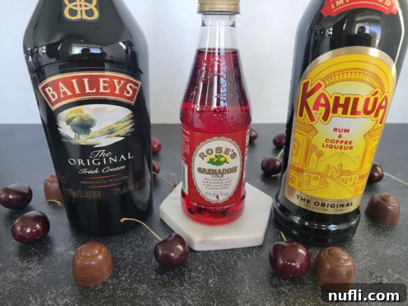 Bottles of Baileys Irish Cream, Grenadine, and Kahlua coffee liqueur are displayed next to fresh chocolate-covered cherries, showcasing the core ingredients for the shot.