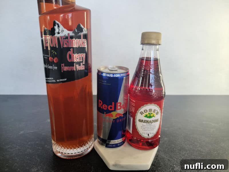 Bottles of cherry vodka, a can of Red Bull energy drink, and a bottle of grenadine syrup, neatly arranged to showcase the essential ingredients.