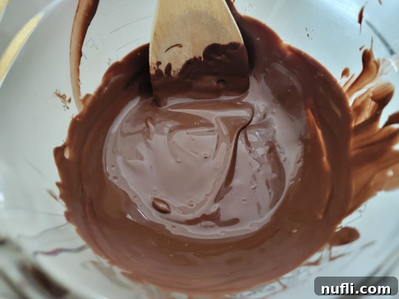 Smooth, melted dark chocolate in a glass microwave-safe bowl with a wooden spoon, ready for dipping crispy potato chips.