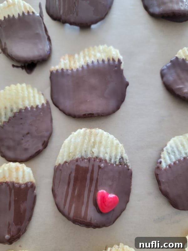 Freshly dipped Ruffles potato chips cooling and setting on parchment paper, displaying their alluring chocolate coating.