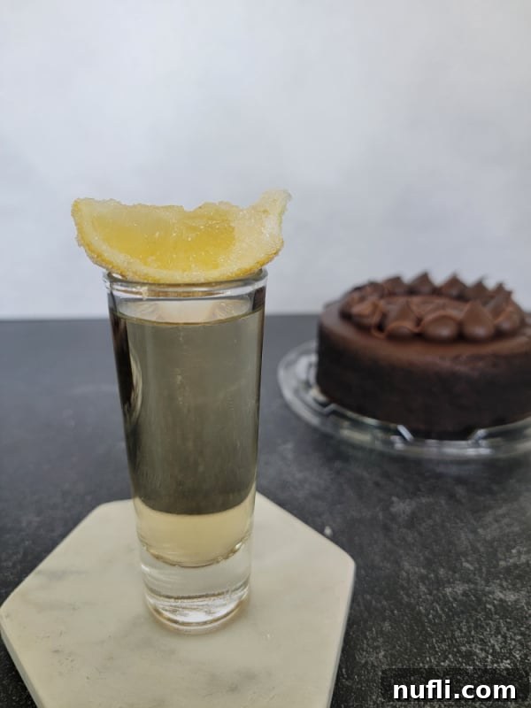 A perfectly prepared Chocolate Cake Shot with a sugar-coated lemon wedge balanced on the rim, ready to be enjoyed alongside a chocolate cake.