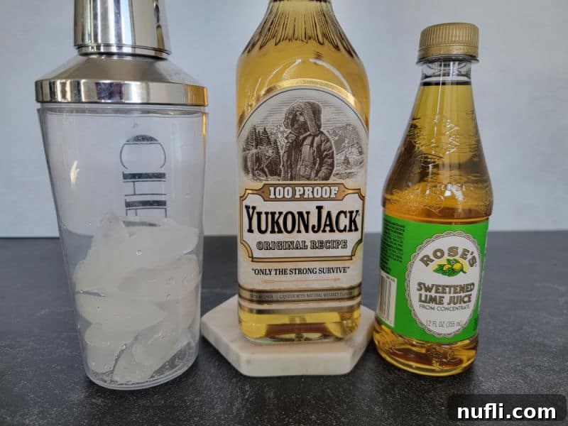 A cocktail shaker filled with ice, a bottle of 100 proof Yukon Jack, and a bottle of Rose's Sweetened Lime Juice, ready for mixing.