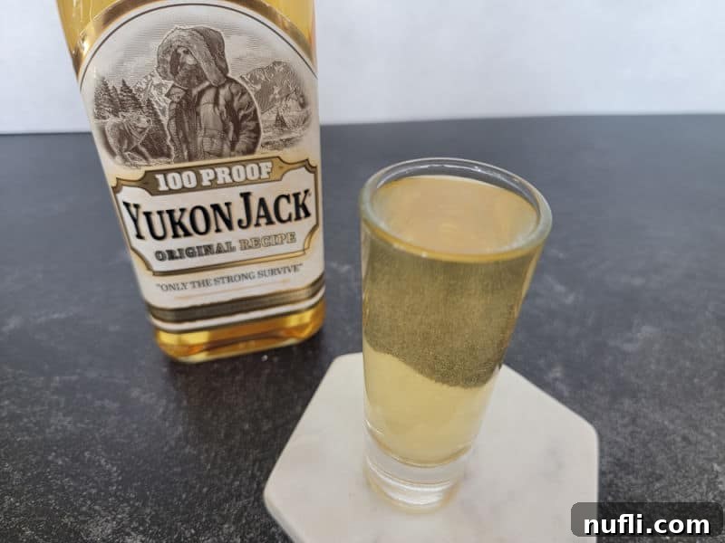 A freshly poured Snakebite Shot in a glass, with the Yukon Jack bottle in the background, ready to be enjoyed.