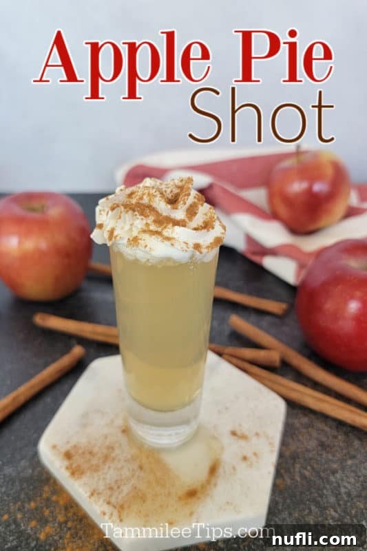 Apple Pie In A Shot Glass 2 Apple Pie Shot over a shot garnished with whipped cream and cinnamon on a white coaster surrounded by cinnamon sticks and apples